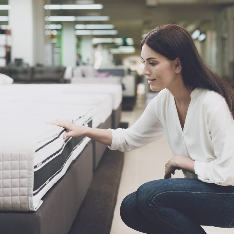 A woman chooses a mattress in a store. She sits next to him and examines him