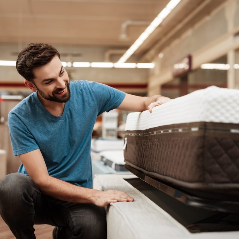 3333881 Young bearded man is testing mattress in furniture store